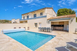Ein zweistöckiges Gebäude mit Swimmingpool, Außenbereich zum Sitzen und Küchenzeile.