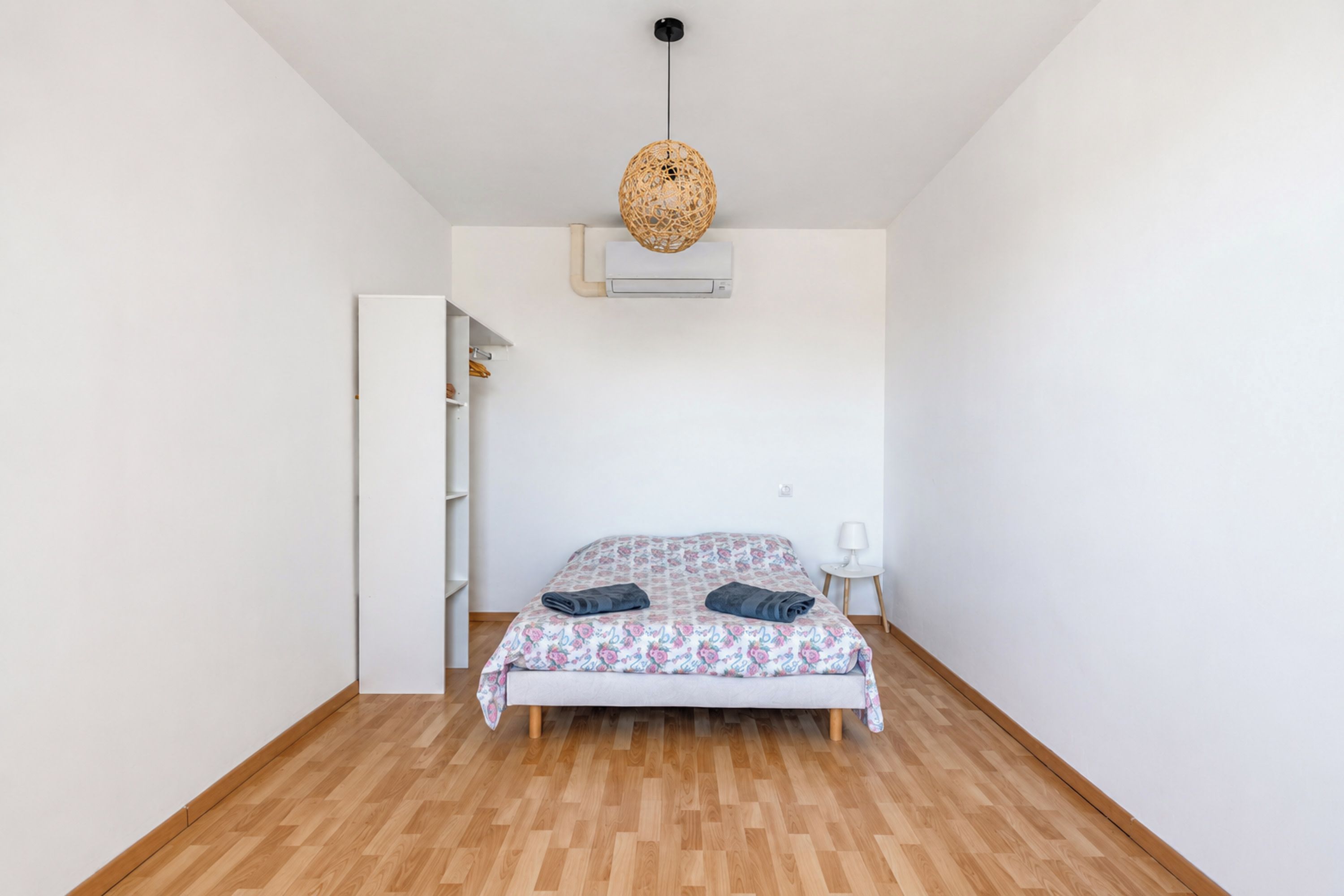 A bedroom with a bed, a white wardrobe, a hanging light fixture, and an air conditioning unit.