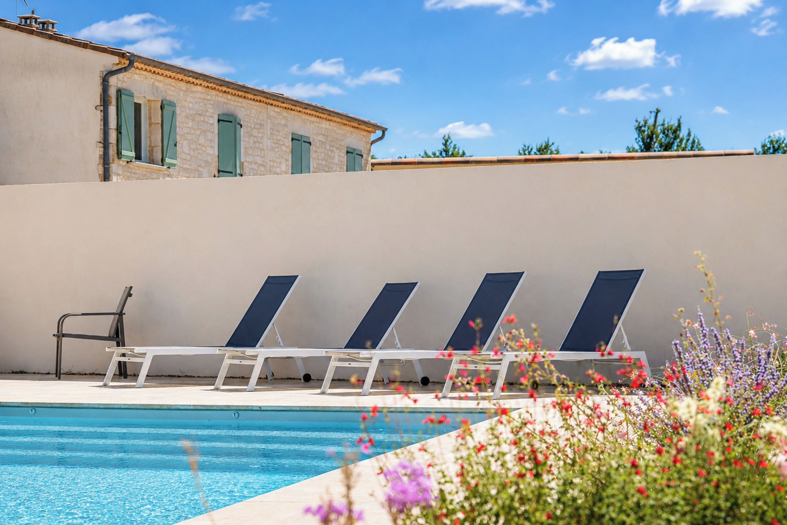 Une piscine avec des chaises longues et, en arrière-plan, un bâtiment aux murs de pierre et aux fenêtres.