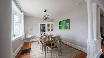 A dining area with a wooden table and chairs, a patterned rug, and a green leaf painting on the wall.