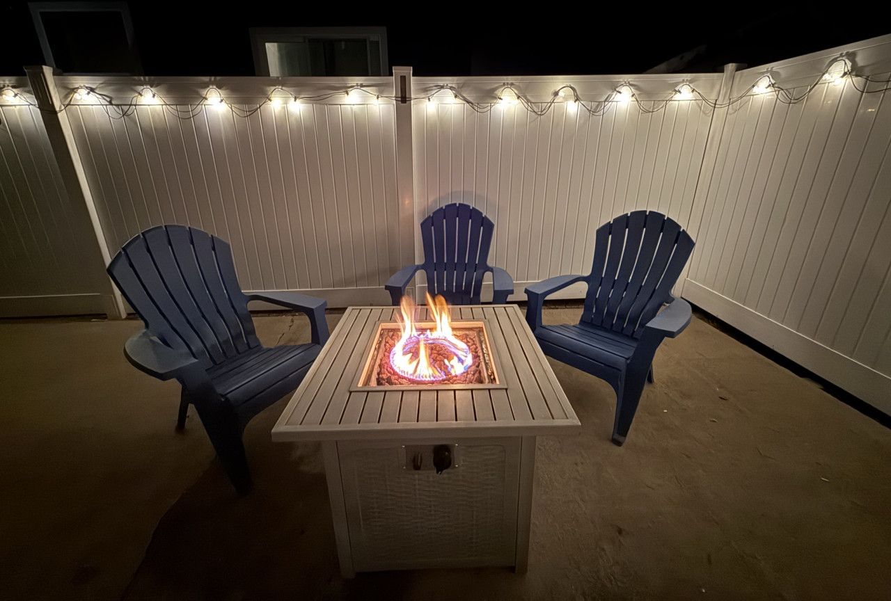 A patio with a square table, two chairs, and a fire pit.