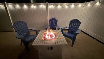 A patio with a square table, two chairs, and a fire pit.