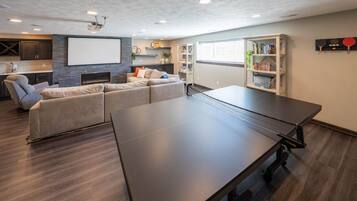 Ein modernes Wohnzimmer mit Tischtennisplatte, einer Couch, einem Bücherregal und einer Projektionsleinwand.