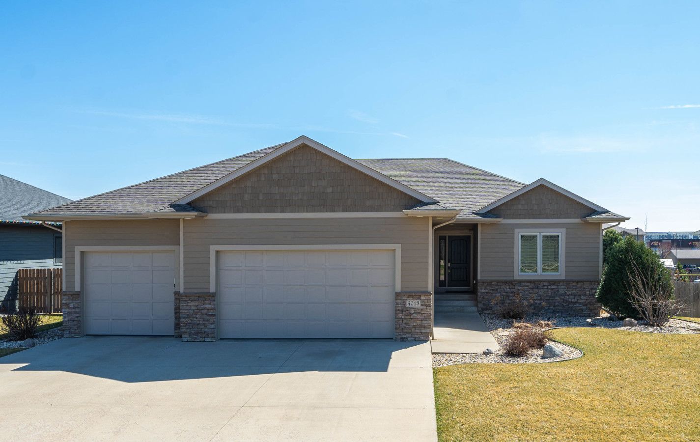 A two-story house with a garage, a stone foundation, and a well-maintained lawn.