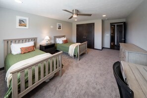 A bedroom with two single beds, a nightstand, a desk, a chair, a wardrobe, and a ceiling fan.