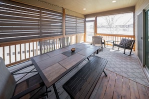 An outdoor patio with a wooden table and chairs, a covered seating area, and a view of a snowy landscape.
