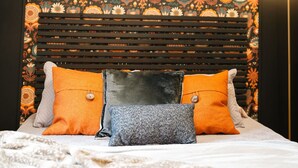 Una cama con un cabecero estampado, dos almohadas naranjas y una almohada gris.