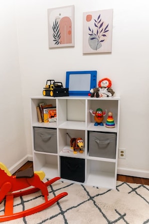 A child's play area with a white shelf unit, a blue TV, and various toys.