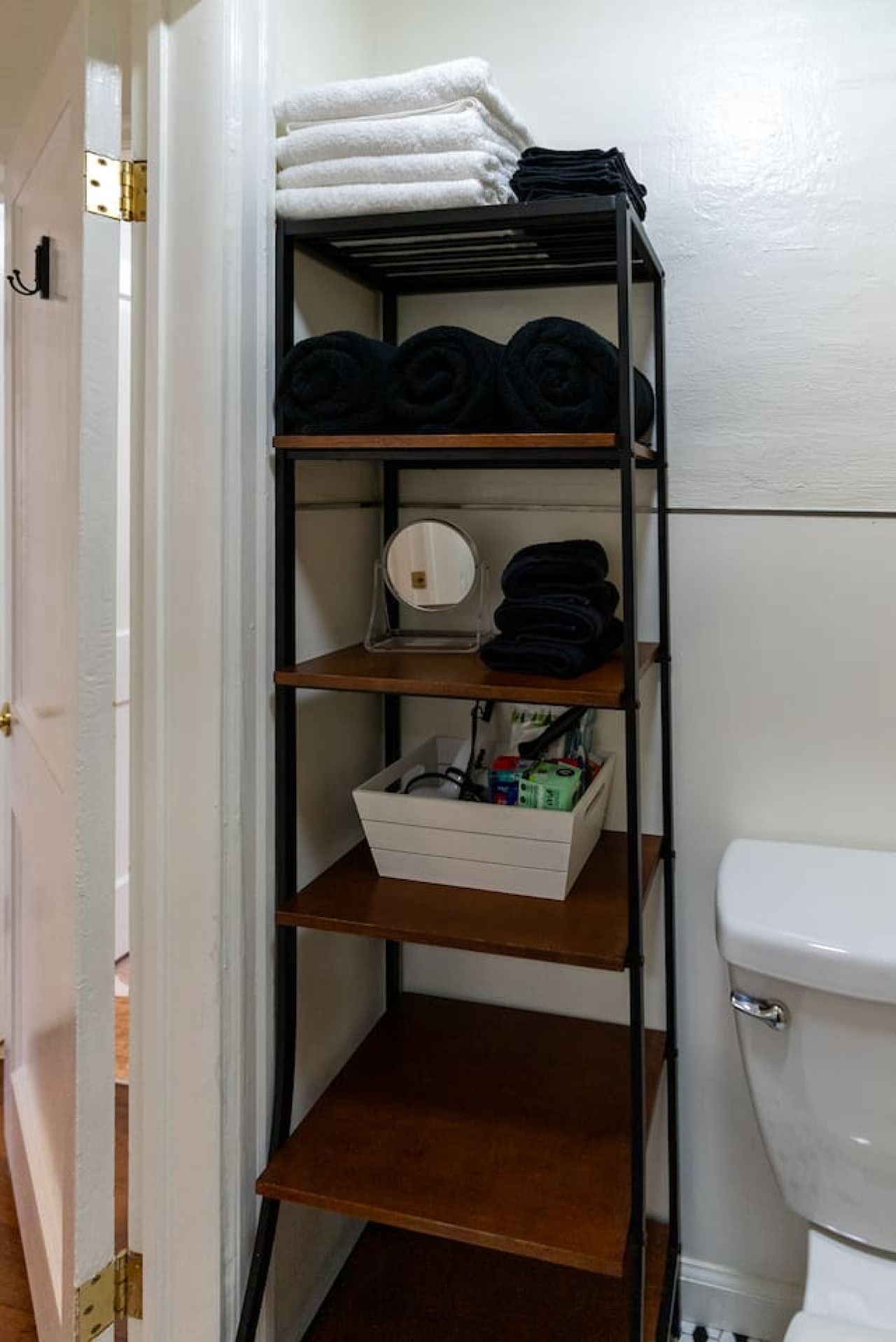 Un couloir étroit, avec une étagère métallique adossée à un mur, contenant des serviettes pliées et un petit miroir.