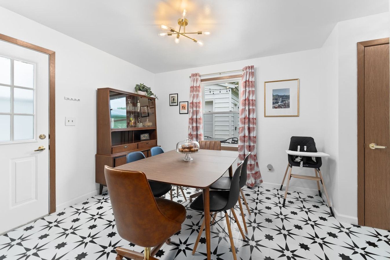 Un coin repas comprenant une table en bois, des chaises, une chaise haute, un buffet et un sol à motifs.