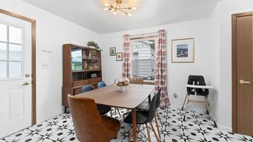 Un coin repas comprenant une table en bois, des chaises, une chaise haute, un buffet et un sol à motifs.