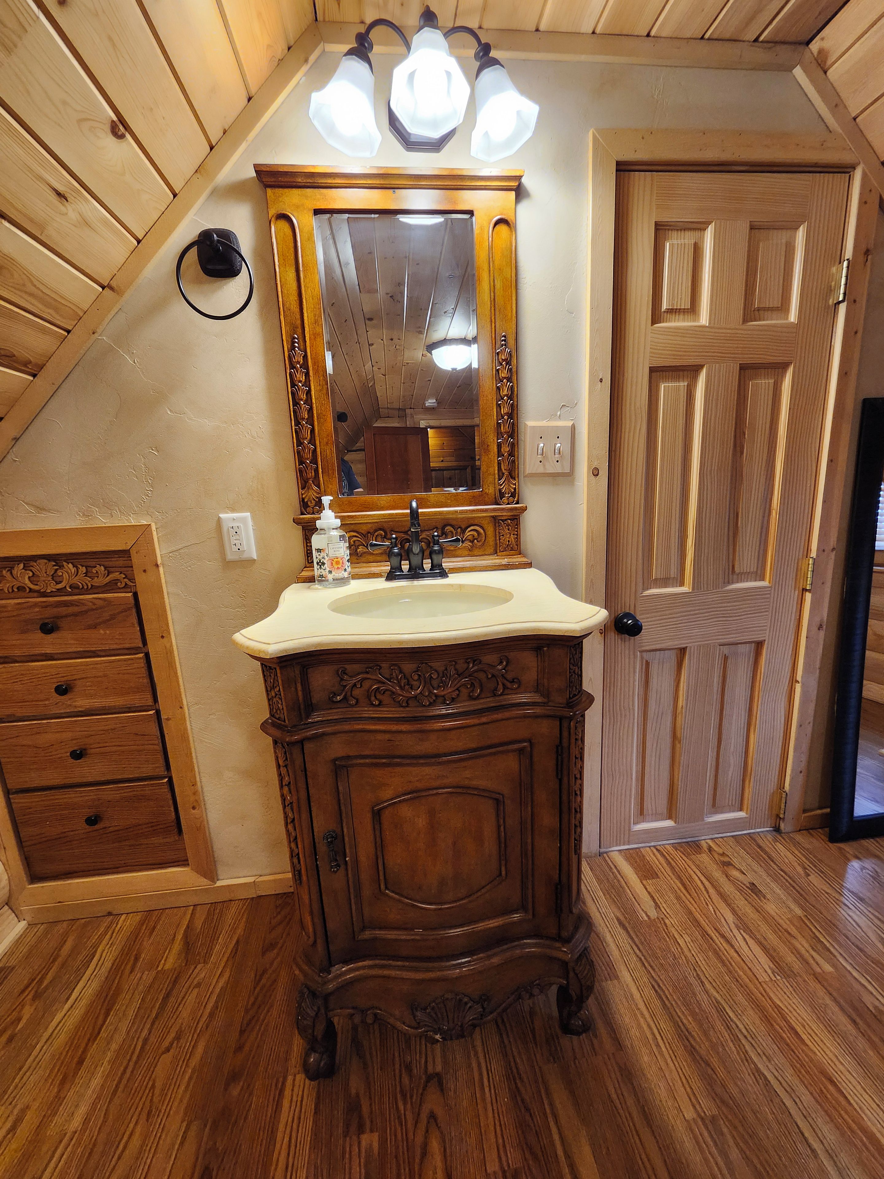 Un baño con tocador de madera, lavamanos, espejo y puerta.