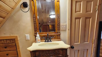 Un baño con tocador de madera, lavamanos, espejo y puerta.