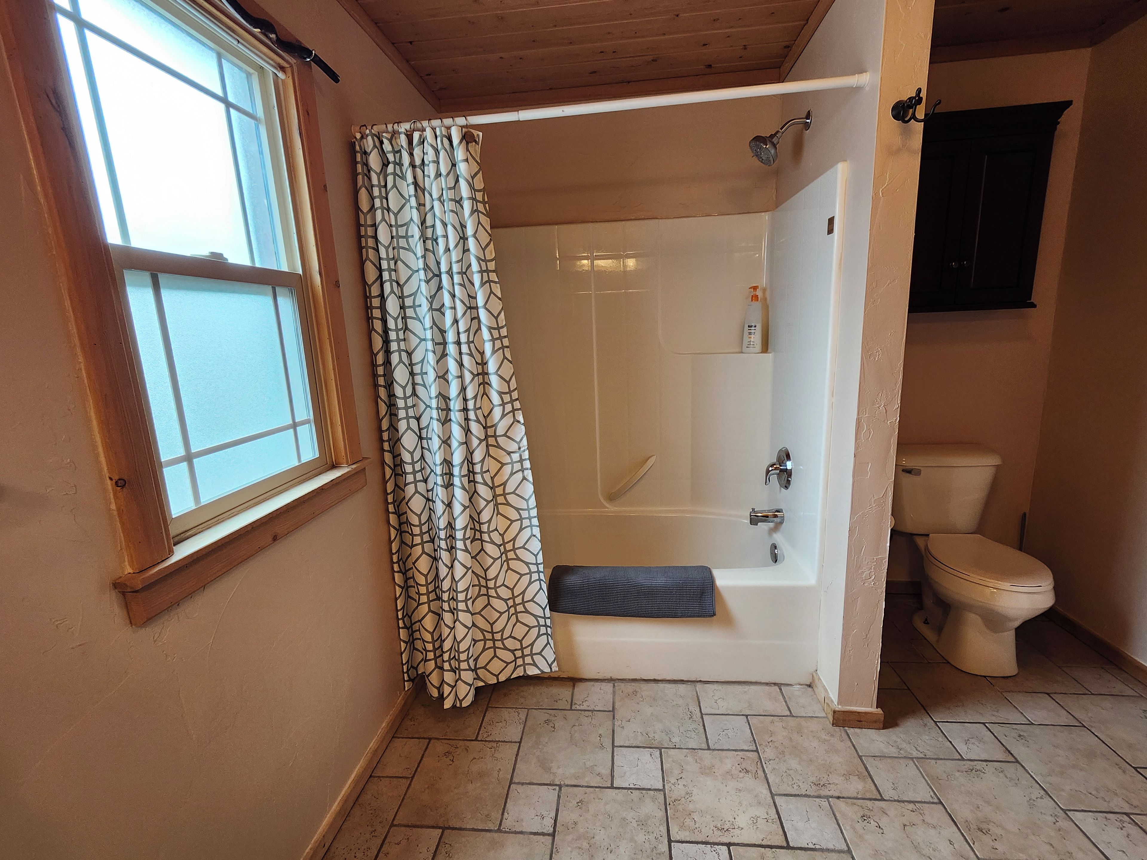 A bathroom with a shower, toilet, and a window.