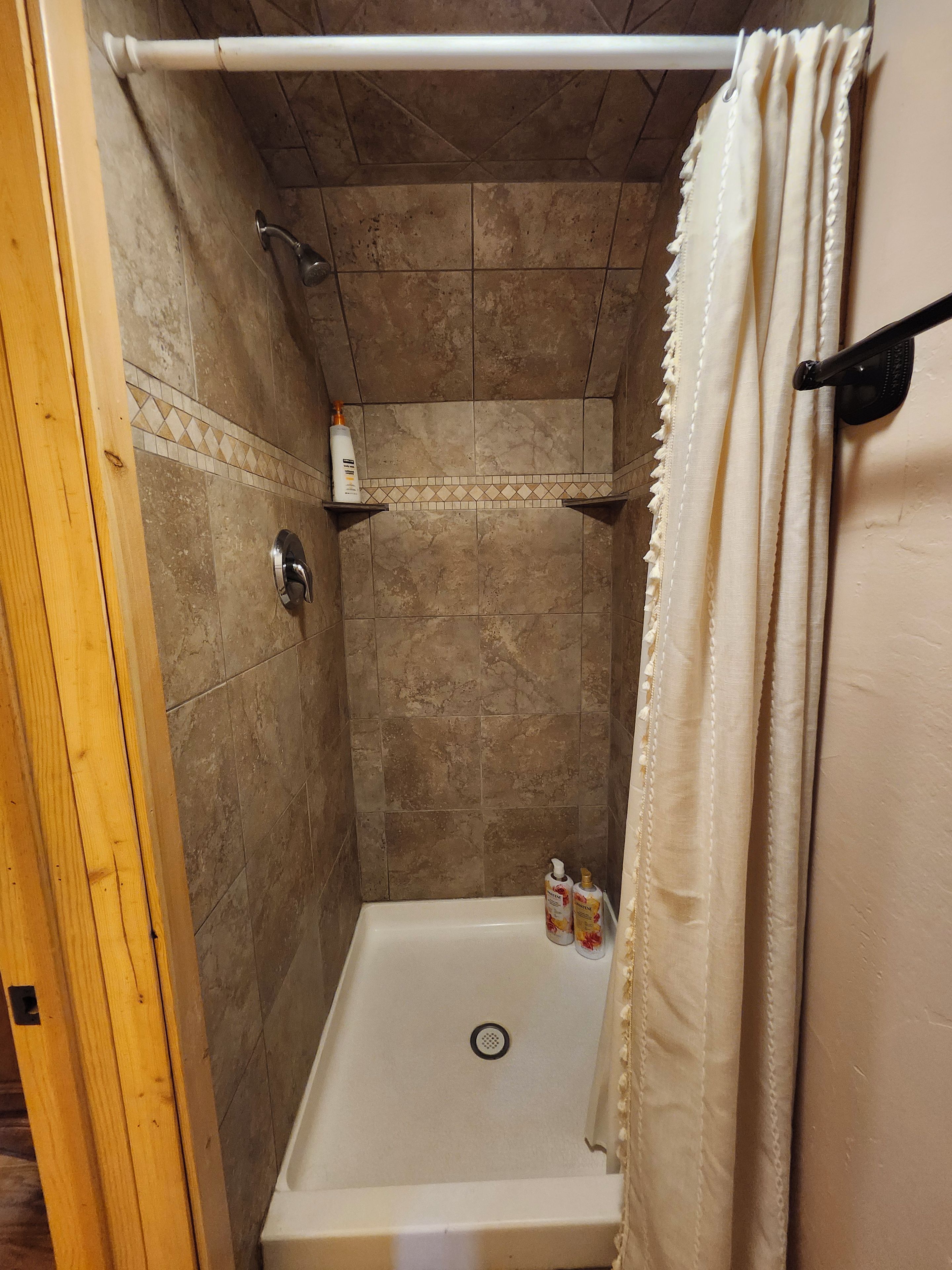 A shower with a drain, tiled walls, and a wooden door frame.