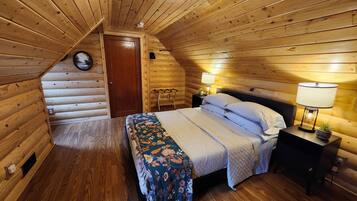 Un dormitorio acogedor tipo cabaña de madera, con cama, lámparas de noche y techo de madera.