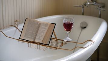 Une baignoire, un livre et un verre de vin rouge posés sur une étagère métallique.