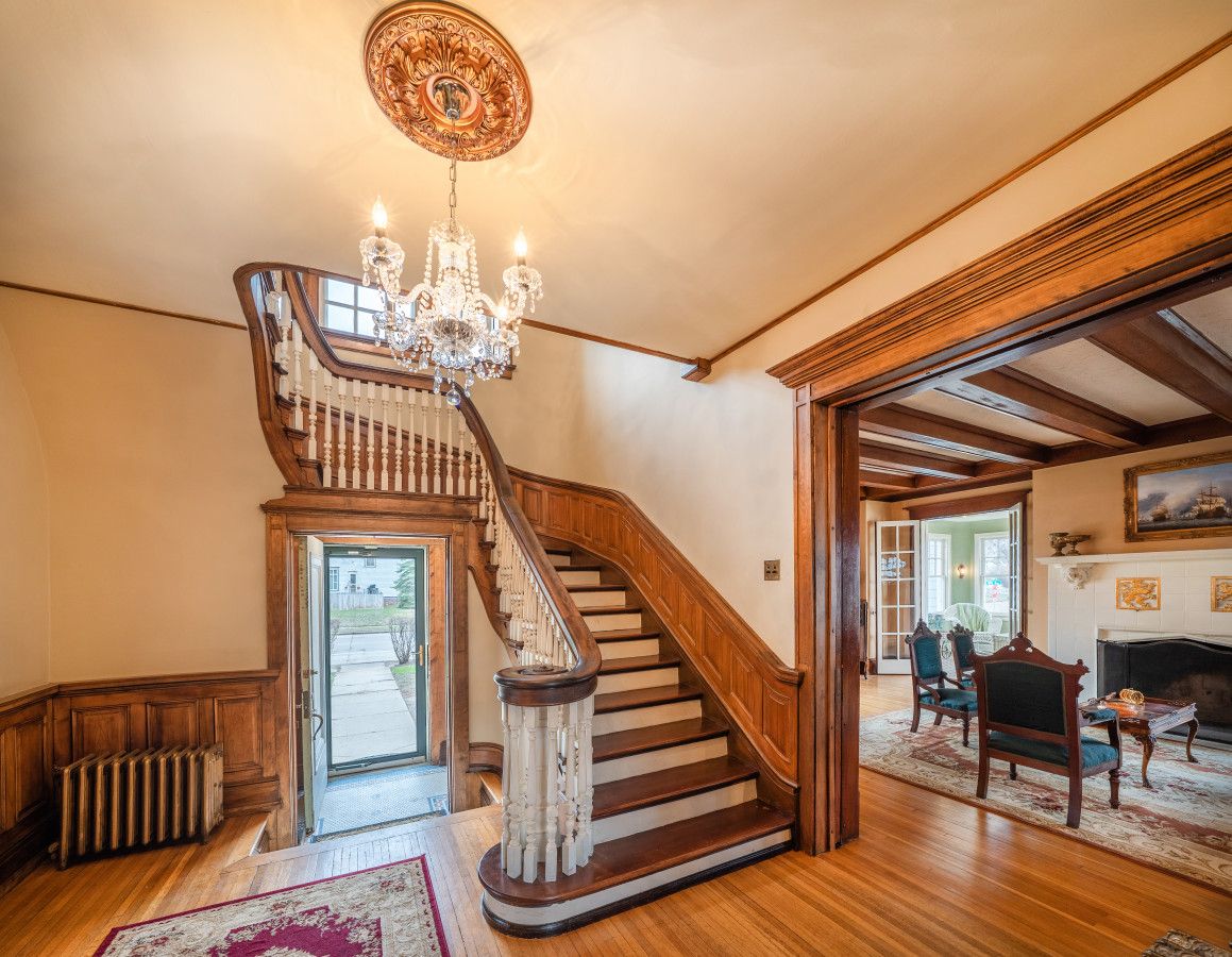 Una imponente escalera con candelabro, pisos de madera y chimenea en un amplio salón.