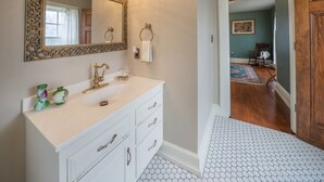 Un baño con tocador blanco, un espejo grande con marco ornamentado y un piso de patrón hexagonal.