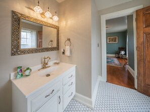 A bathroom with a white vanity, a large mirror with an ornate frame, and a hexagonal patterned floor. - Perry Mansion | Dutch Colonial (Sioux Falls)