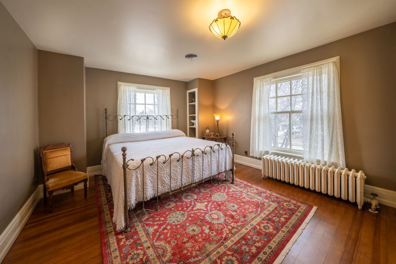 A bedroom with a bed, a chair, a radiator, and a window.