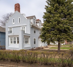 A two-story house with a chimney, a large tree in front, and a well-maintained lawn. - Perry Mansion | Dutch Colonial (Sioux Falls)