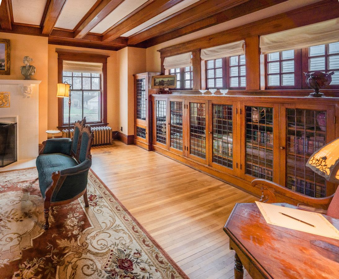 A room with a fireplace, a wooden cabinet with glass doors, a blue armchair, and a patterned rug.