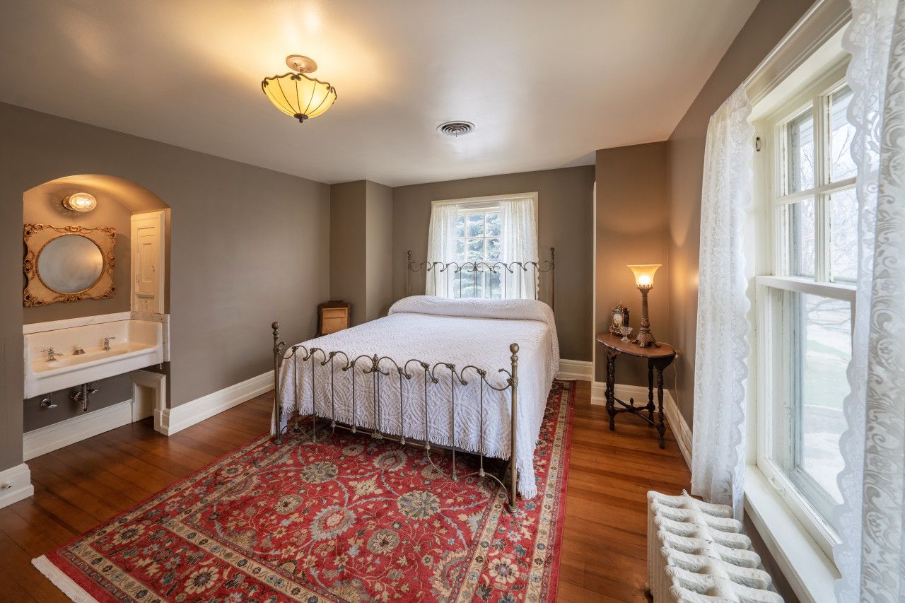 A bedroom with a bed, a nightstand, a dresser, a window with curtains, and a patterned rug.
