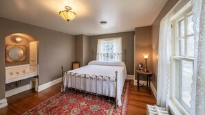 Un dormitorio con cama, mesita de noche, cómoda, ventana con cortinas y una alfombra estampada.