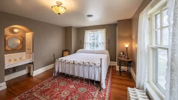 A bedroom with a bed, a nightstand, a dresser, a window with curtains, and a patterned rug.