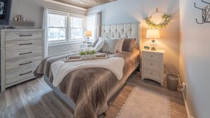 A bedroom with a large bed, a bedside table with a lamp, a dresser, and a window with a view. - Duluth Charmer - 3B/2B cozy home (Sioux Falls)