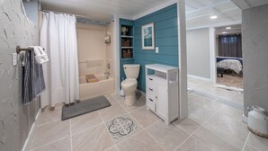 A bathroom with a bathtub, toilet, and sink, featuring a blue accent wall and a patterned floor mat. - Duluth Charmer - 3B/2B cozy home (Sioux Falls)