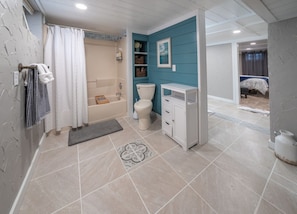 Ein Badezimmer mit Badewanne, Toilette und Waschbecken, mit einer blauen Akzentwand und einer teppichartigen Fußmatte.