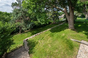 A grassy outdoor area with a stone border, a wooden deck, and trees.