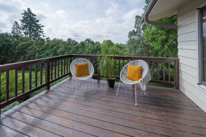 Eine Holzterrasse mit zwei weißen Stühlen aus Draht und gelben Kissen, sowie einem Blumentopf.