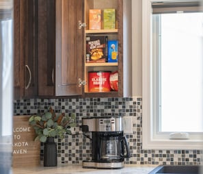 A kitchen with wooden cabinets, a coffee maker, and a welcome sign. - Dakota Haven: Family-Friendly, Clean, Sleeps 8 (Sioux Falls)