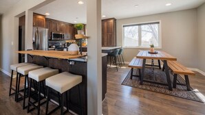 A modern kitchen with a bar area, wooden flooring, and a dining space with a bench and chairs. - Dakota Haven: Family-Friendly, Clean, Sleeps 8 (Sioux Falls)