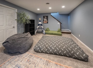A home interior with a carpeted floor, a bean bag, a patterned rug, a ladder, and a green couch. - Dakota Haven: Family-Friendly, Clean, Sleeps 8 (Sioux Falls)