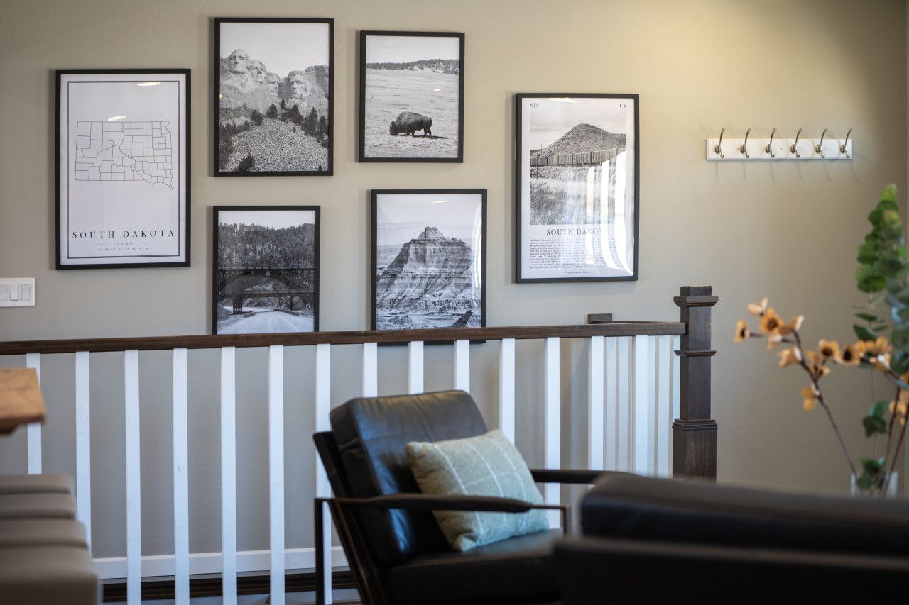 Een kamer met een witte balustrade, een zwarte leren fauteuil met kussen, en een muur versierd met zwart-wit foto's in lijsten.