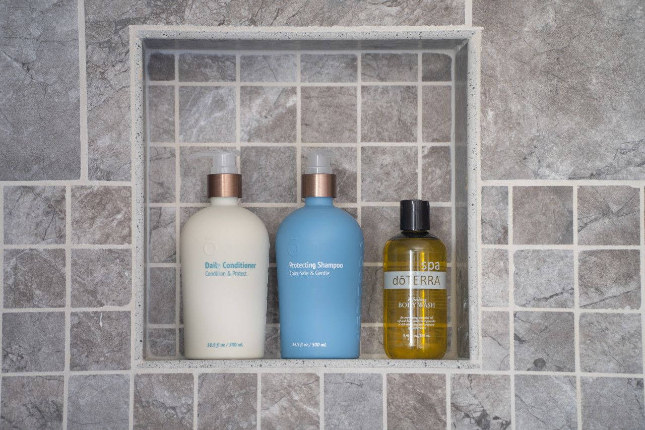 Three bottles of personal care products in a tiled shelf.