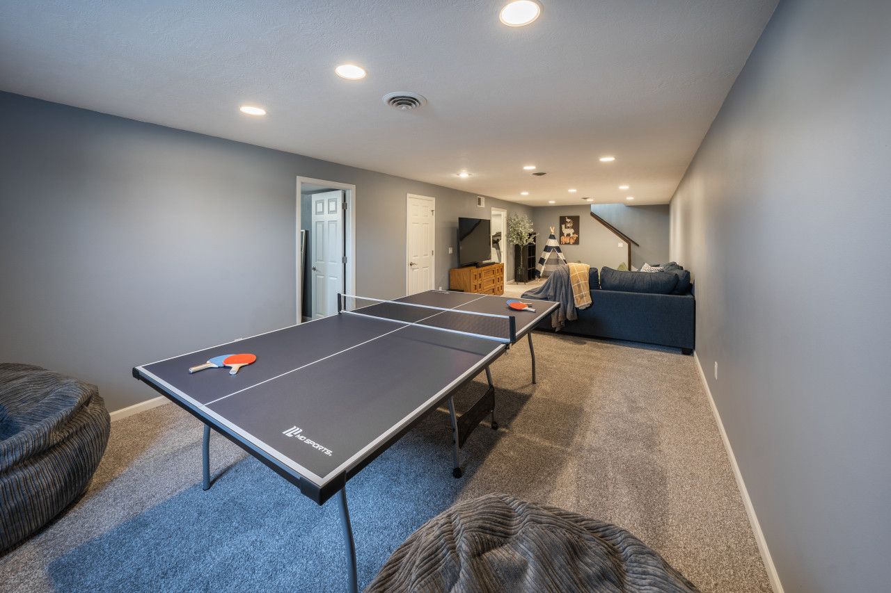 Taula de ping-pong en una habitació amb una decoració en tons neutres, un sofà i una porta que dona a un altre espai.