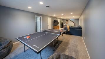 Taula de ping-pong en una habitació amb una decoració en tons neutres, un sofà i una porta que dona a un altre espai.