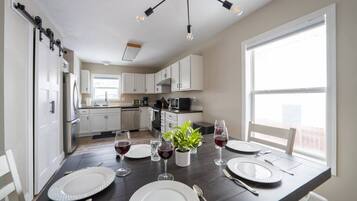 A modern kitchen with white cabinets, a dining table set for two with plates, glasses, and cutlery, and a potted plant on the table.