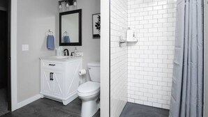 Ein Badezimmer mit begehbarer Dusche, Toilette, Waschbecken und Spiegel.