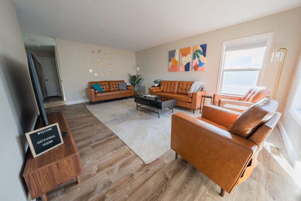 Ein modernes Wohnzimmer mit Ledersofas, einem Couchtisch und einem Fernseher. Ein Willkommensschild steht auf einem Holzboden.