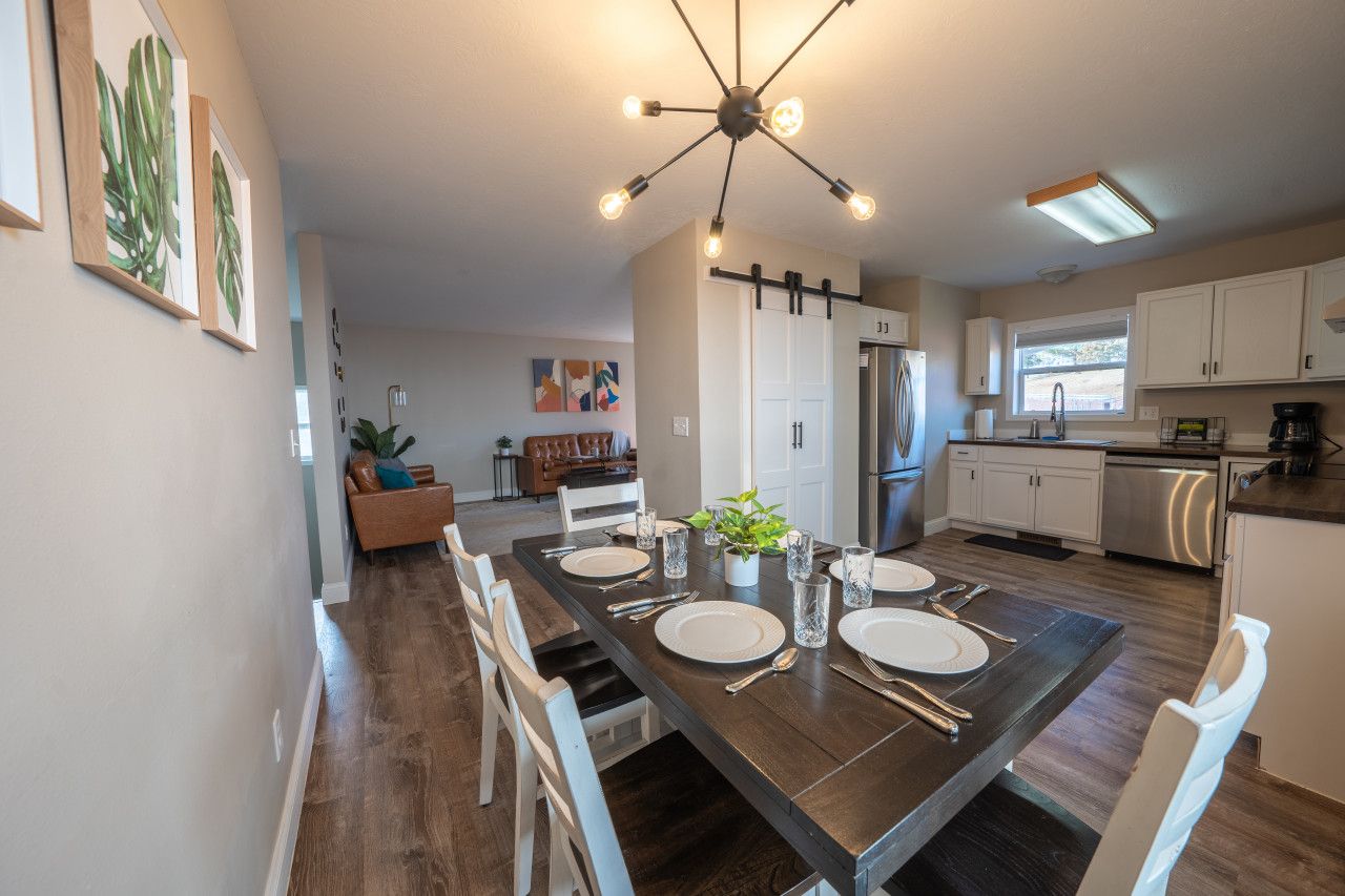A modern kitchen with a dining area, featuring a dark wooden table set for four, white cabinets, and a stainless steel refrigerator.