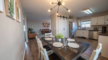 A modern kitchen with a dining area, featuring a dark wooden table set for four, white cabinets, and a stainless steel refrigerator.