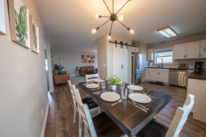 A modern kitchen with a dining area, featuring a dark wooden table set for four, white cabinets, and a stainless steel refrigerator.