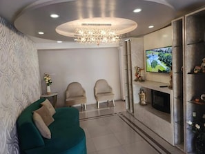 Ein Wohnzimmer mit einer Couch, zwei Sesseln, einem Fernseher und einem Kamin.