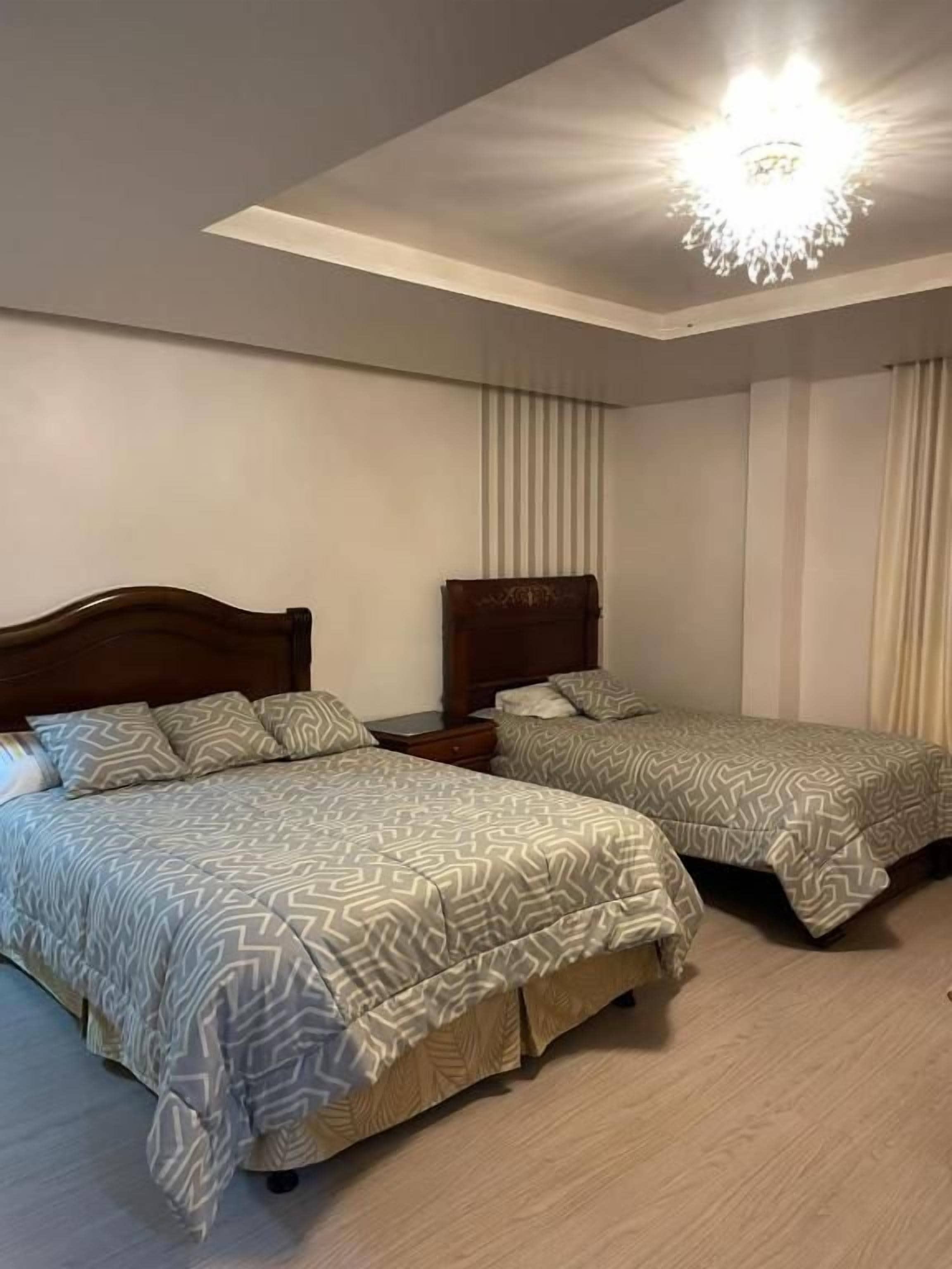 Un dormitorio con dos camas, una araña y un ventanal con cortinas.